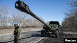 An armed man stands near a truck towing an artillery piece as rebels with the separatist self-proclaimed Donetsk People's Republic Army pull back from Donetsk, Ukraine, Feb. 24, 2015.